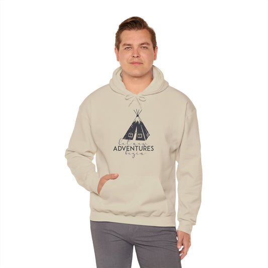 A person wearing a beige unisex hooded sweatshirt with 'Adventures' text and a Native American-inspired design on the front.
