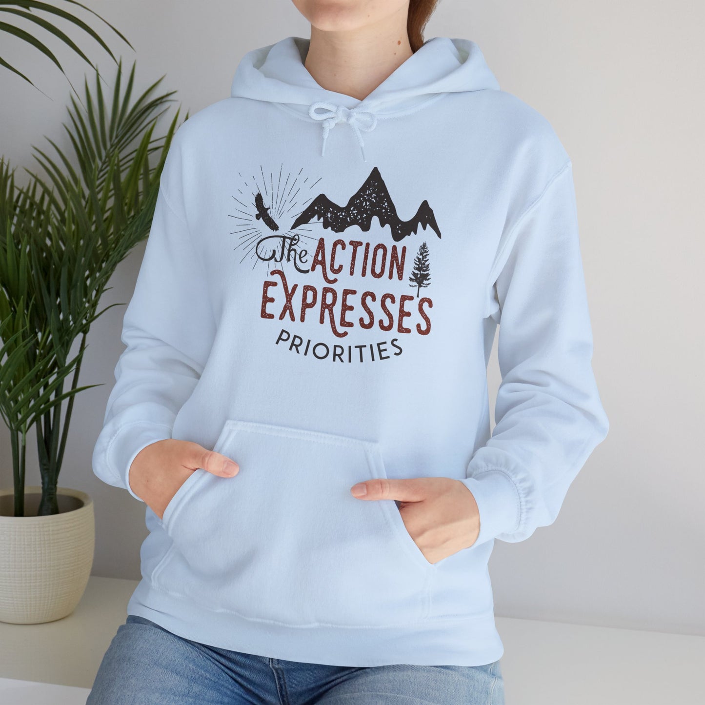 A person wearing a light blue unisex hooded sweatshirt with 'The Action Expresses Priorities' printed on the front.