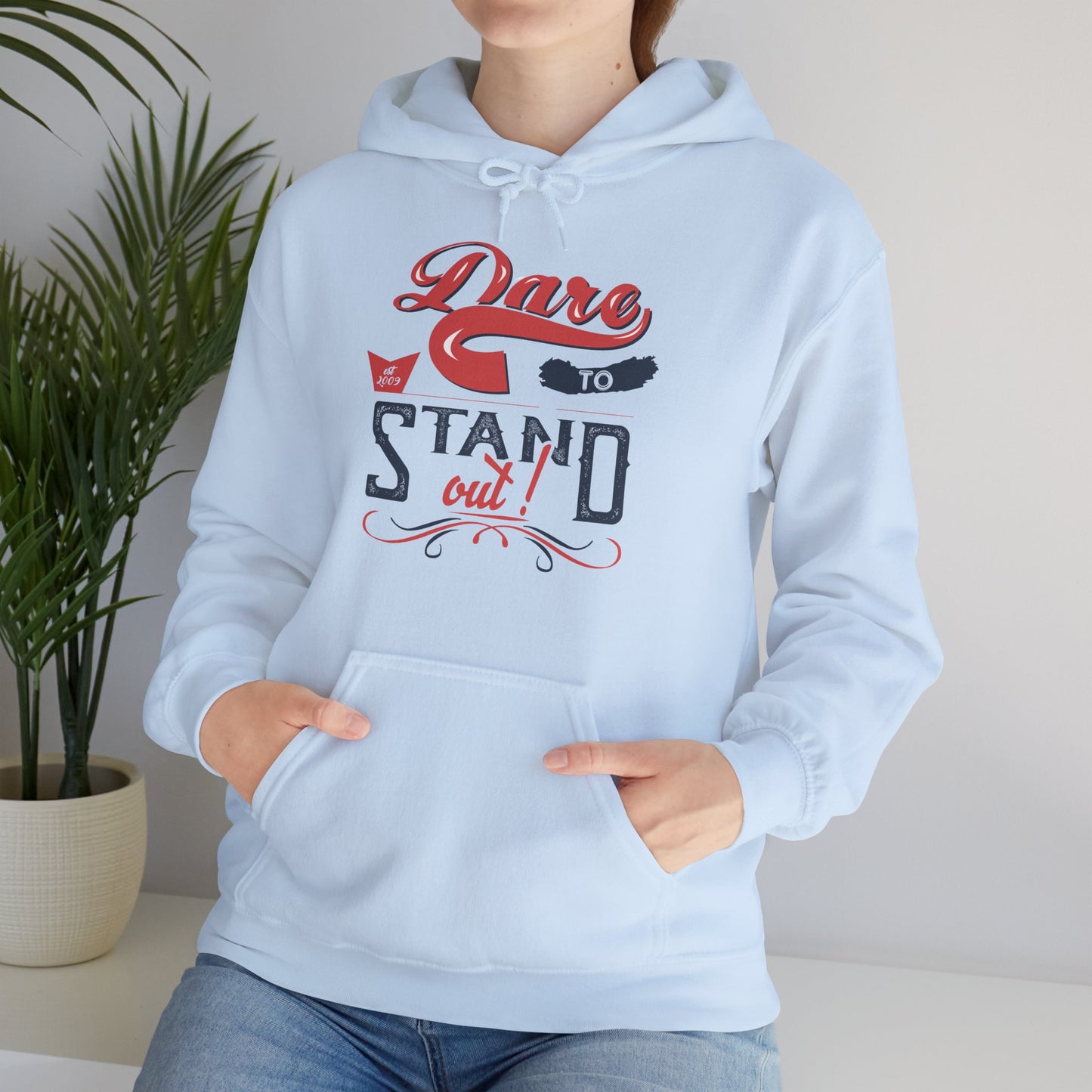 A person wearing a blue unisex hooded sweatshirt with 'Dare To Stand Out!' text and a graphic design.