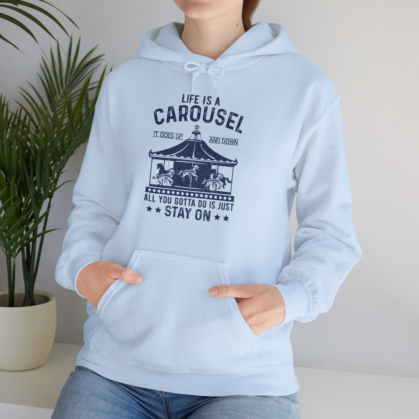 A person wearing a blue unisex hooded sweatshirt with 'Life Is A Carousel' text and carnival-themed graphics.