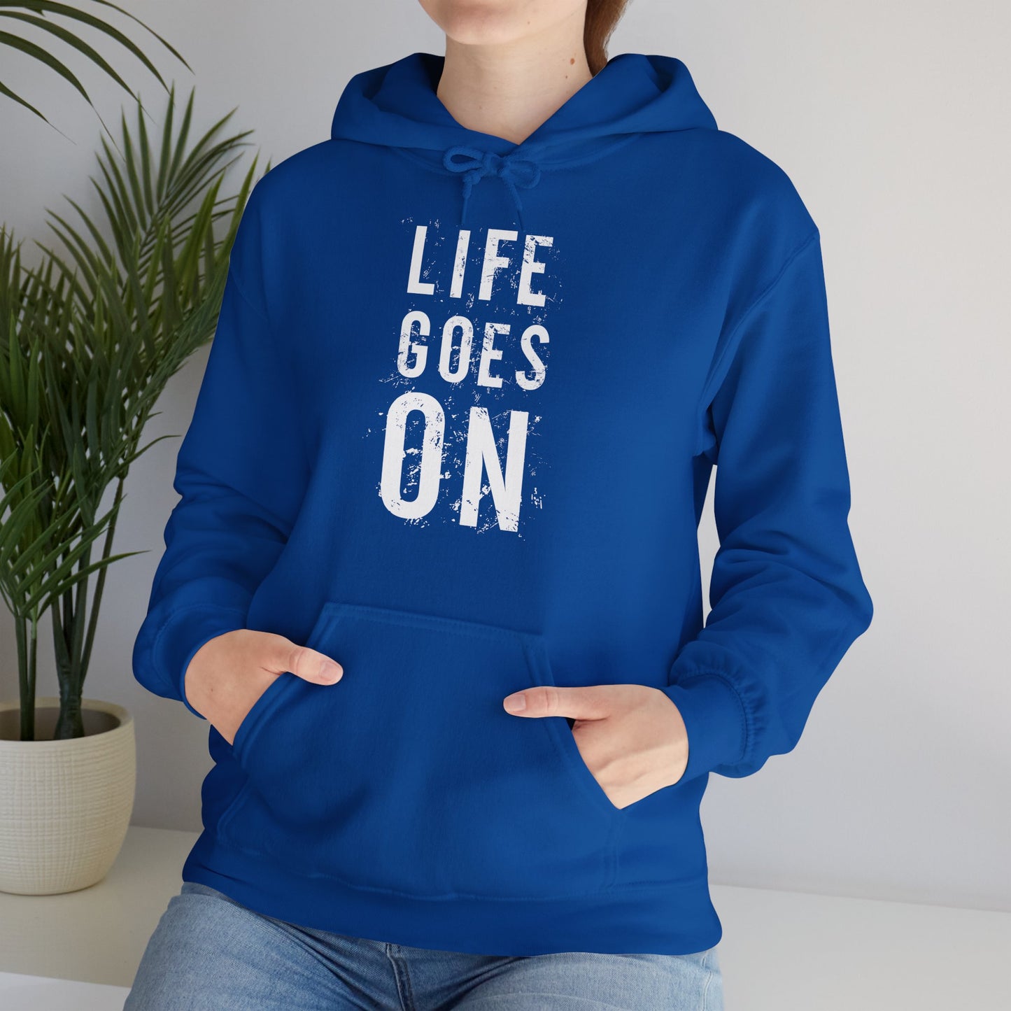 A person wearing a blue unisex hooded sweatshirt with the text 'LIFE GOES ON' printed in white on the front.