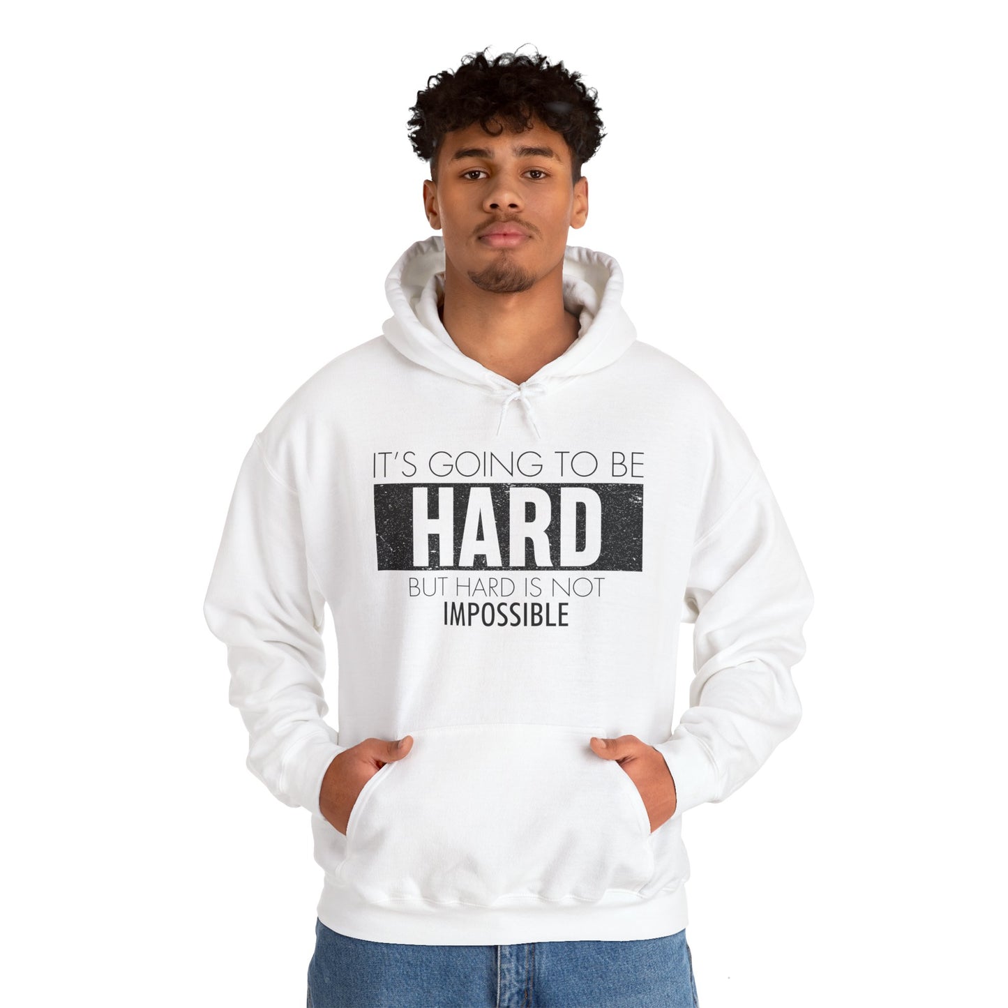 A male model wearing a white unisex hooded sweatshirt with the text 'It's Going To Be Hard BUT NOT IMPOSSIBLE' printed on the front.