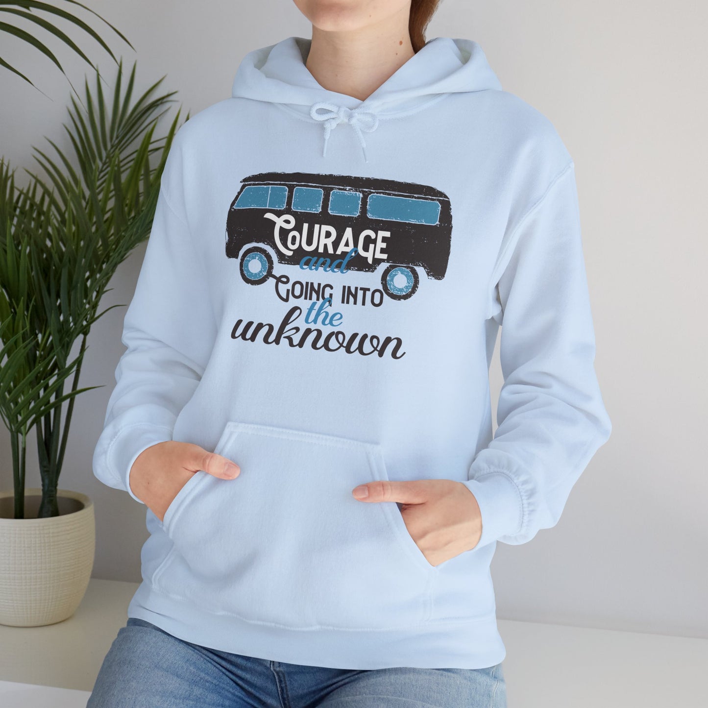 A person wearing a light blue unisex hooded sweatshirt with 'Courage Going Into The Unknown' printed on the front.