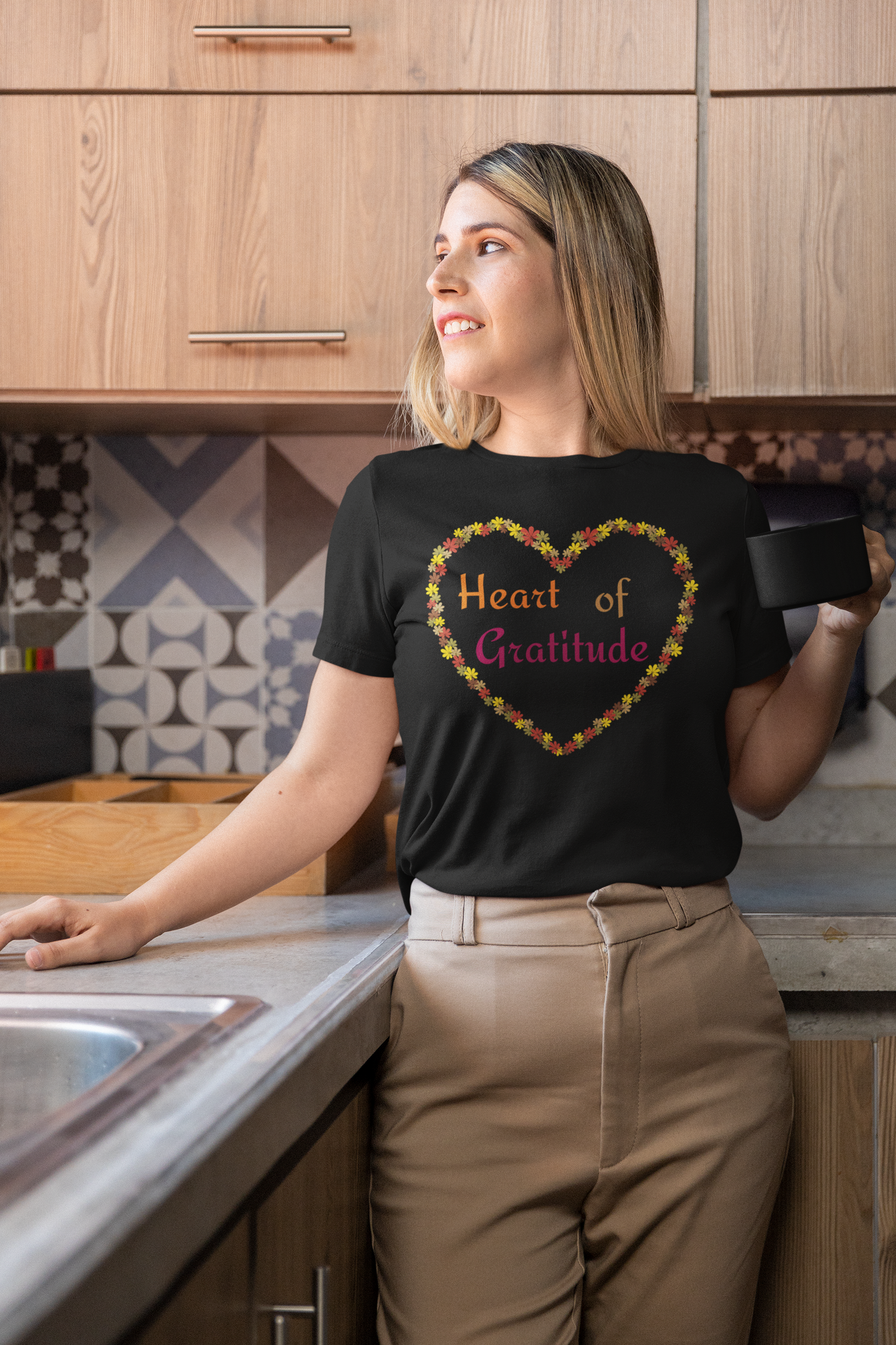 Woman holding coffee mug and wearing a black color motivational t-shirt design displaying heart of gratitude.