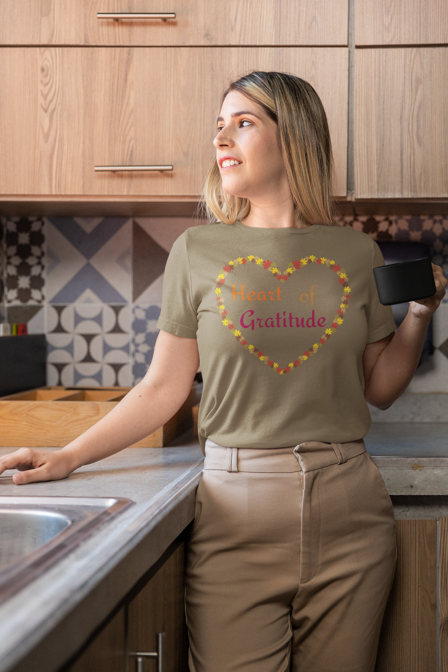 Woman holding coffee mug and wearing a heather olive color motivational t-shirt design displaying heart of gratitude.