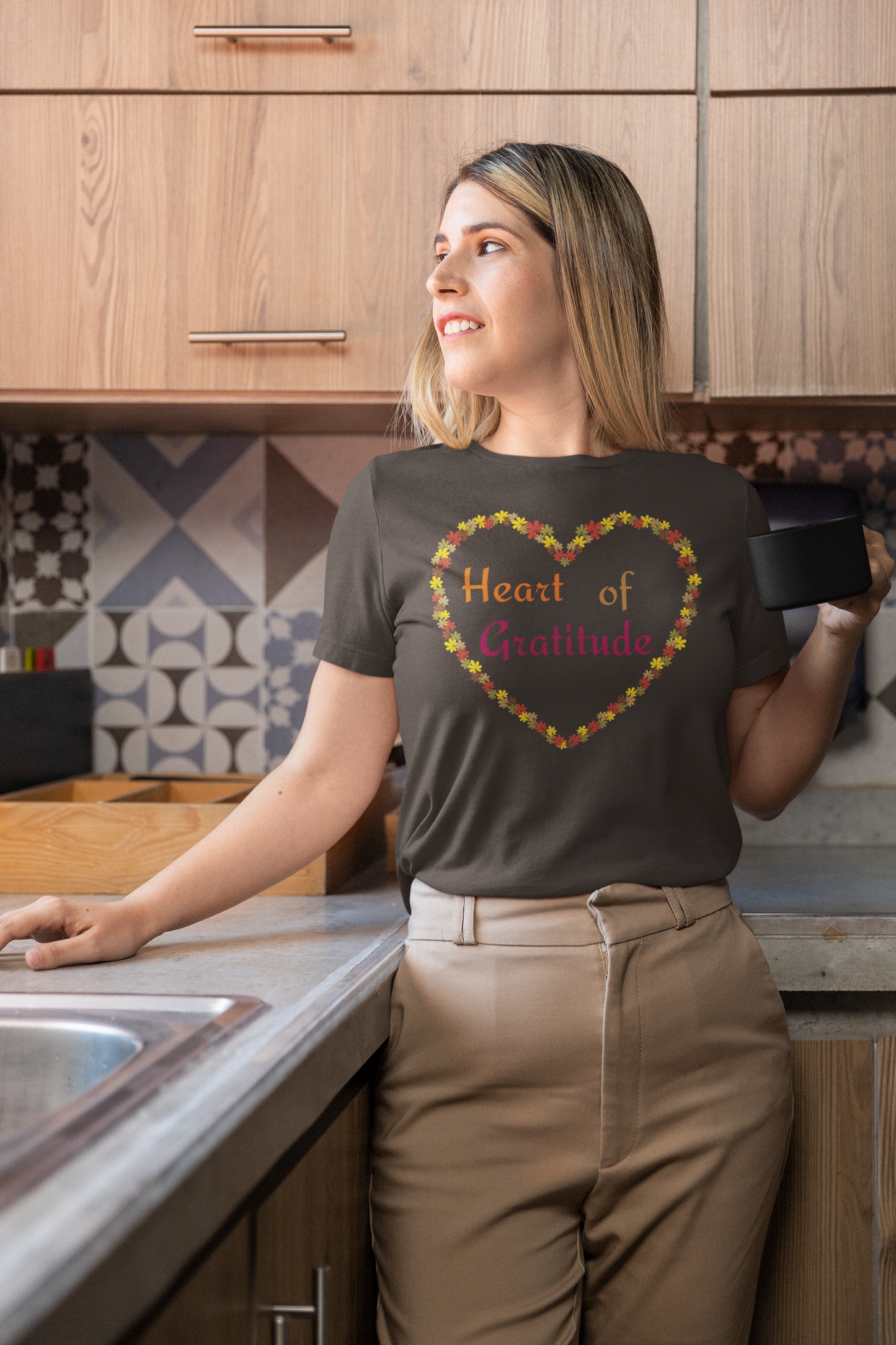 Woman holding coffee mug and wearing a brown color motivational t-shirt design displaying heart of gratitude.