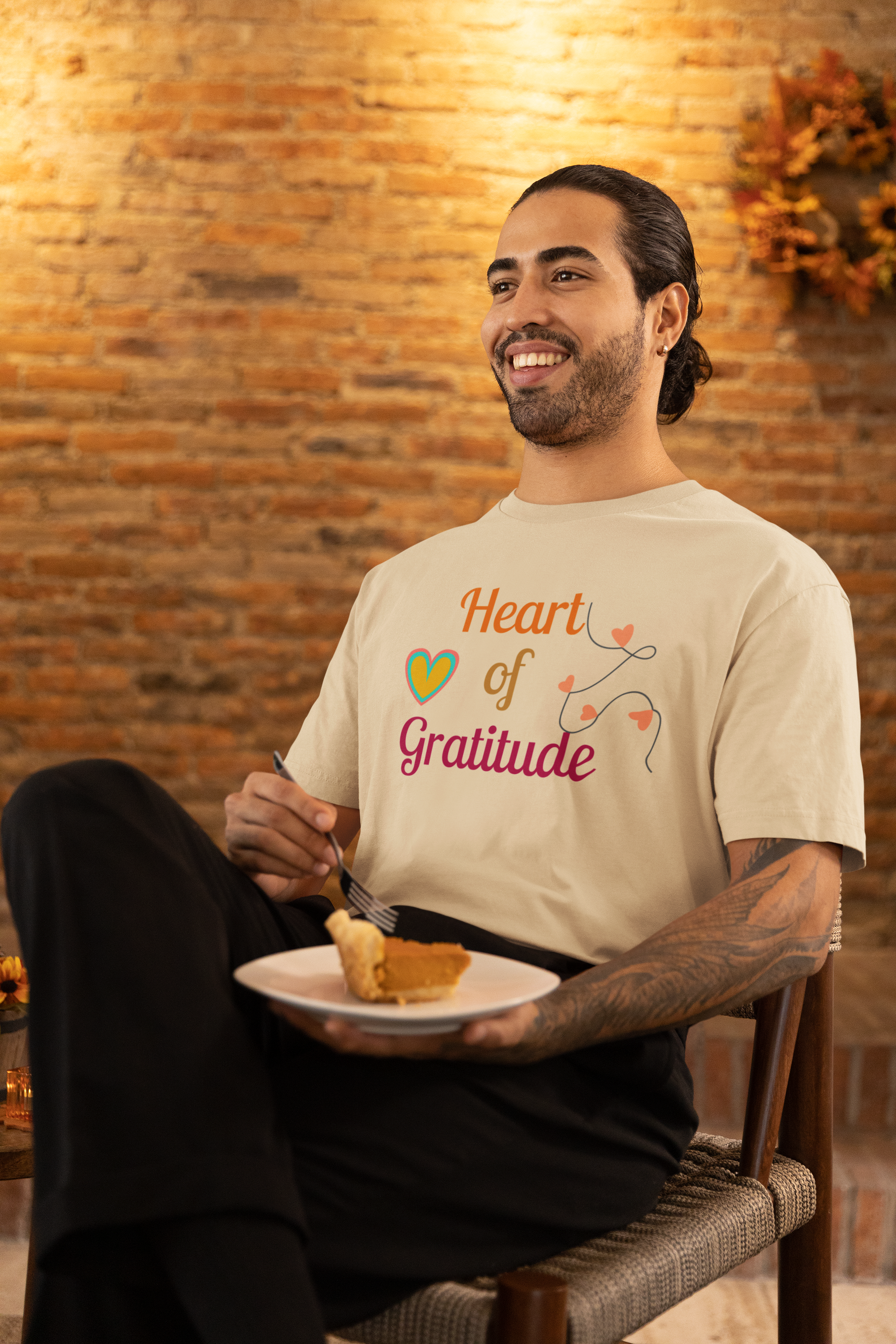 Man with arm tattoo eating pumpkin pie and wearing a soft cream color motivational t-shirt design displaying heart of gratitude.