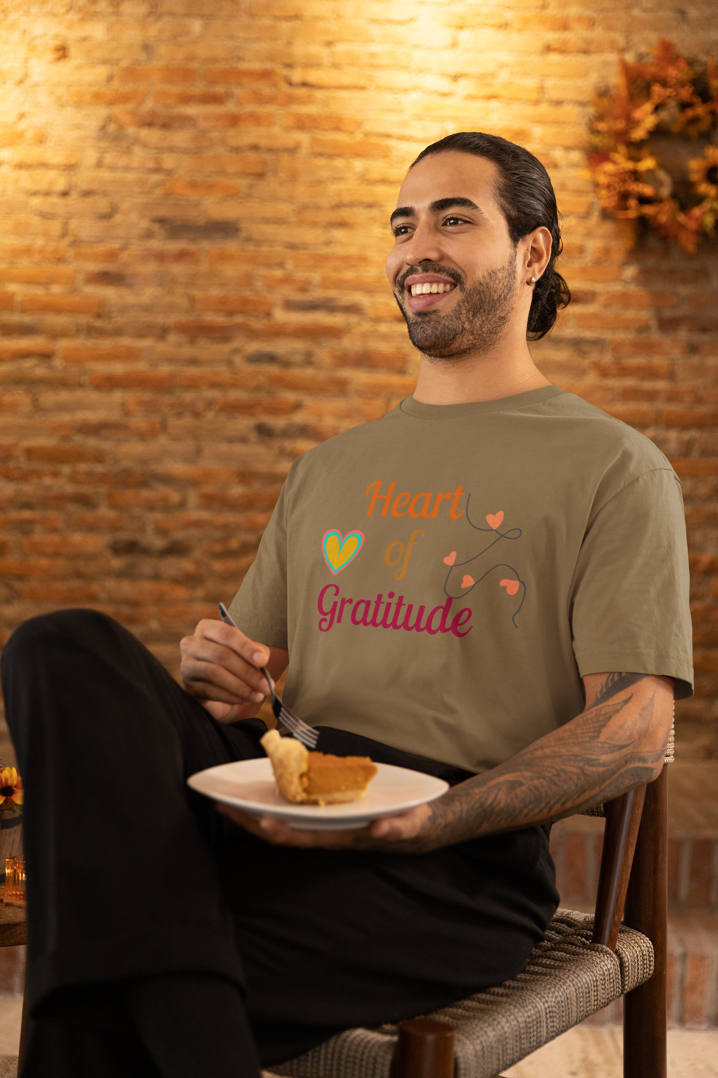 Man with arm tattoo eating pumpkin pie and wearing a heather olive color motivational t-shirt design displaying heart of gratitude.