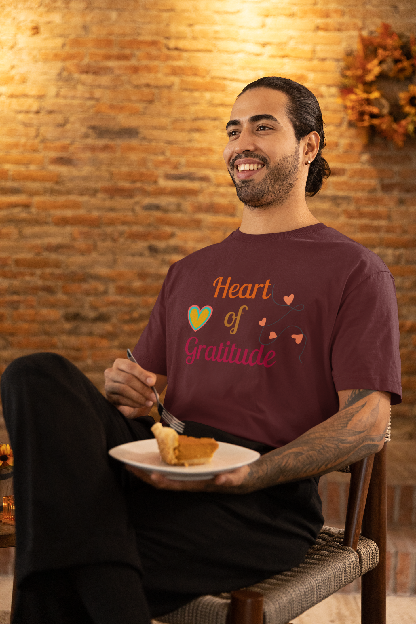 Man with arm tattoo eating pumpkin pie and wearing a maroon color motivational t-shirt design displaying heart of gratitude.