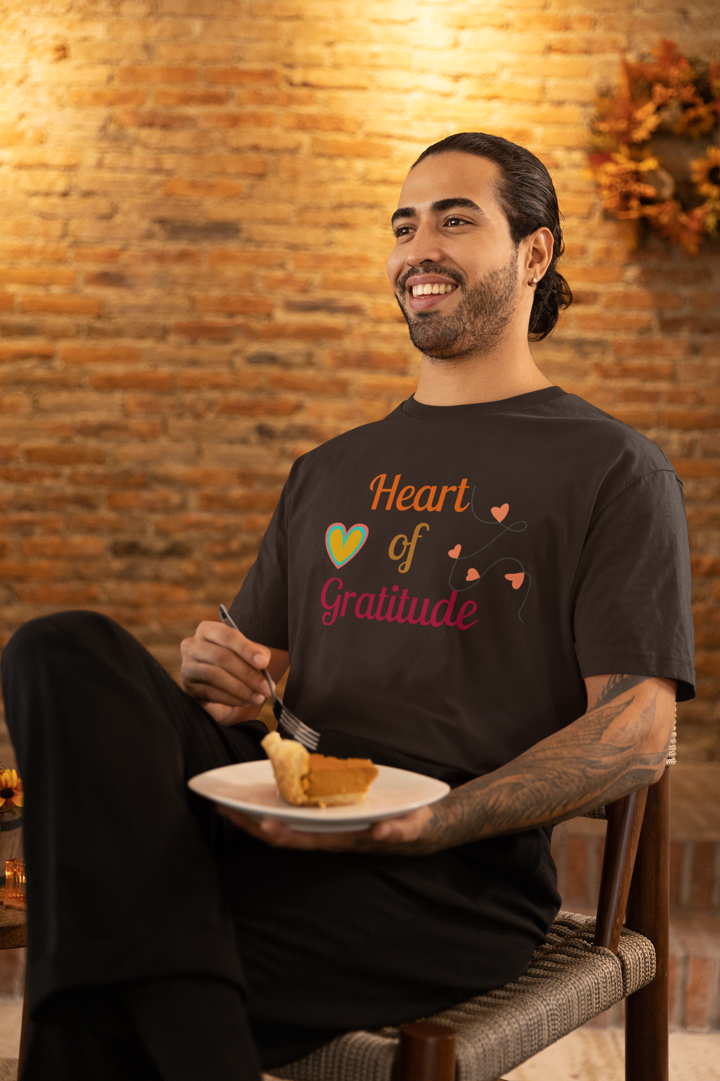 Man with arm tattoo eating pumpkin pie and wearing a brown color motivational t-shirt design displaying heart of gratitude.